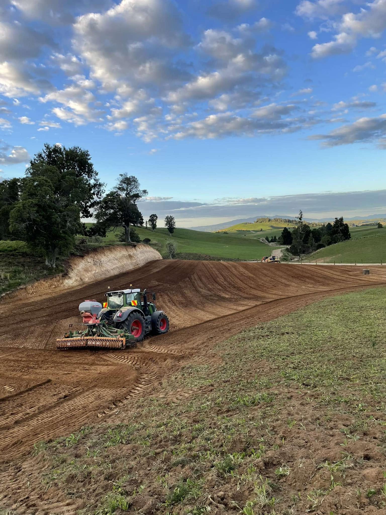 Fendt tractor working ground with a power harrow and air seeder across a large cultivated hill paddock in the evening light