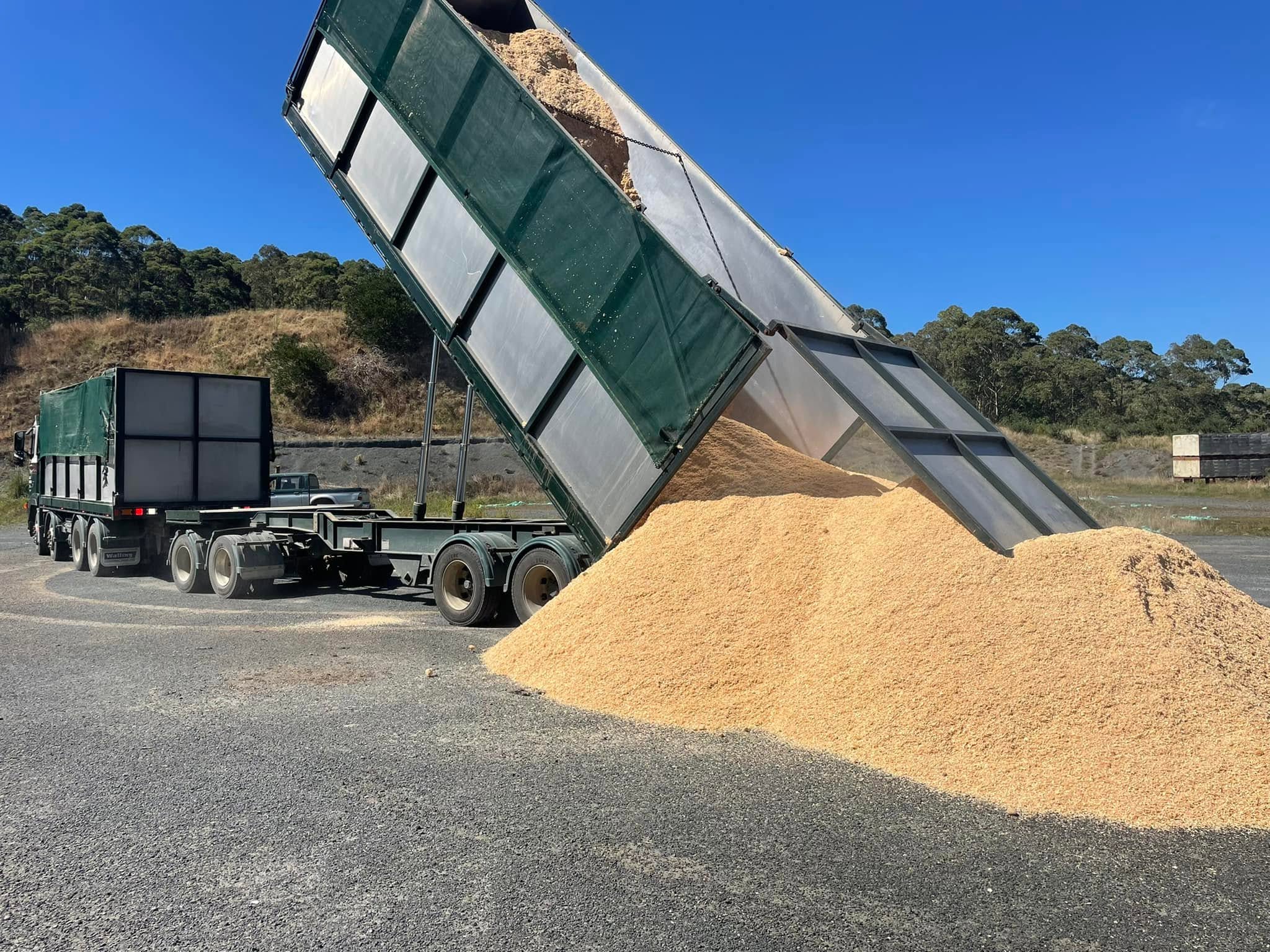 Truck and trailer unit tipping a load of feed into a pile on a hardstand under a clear blue sky
