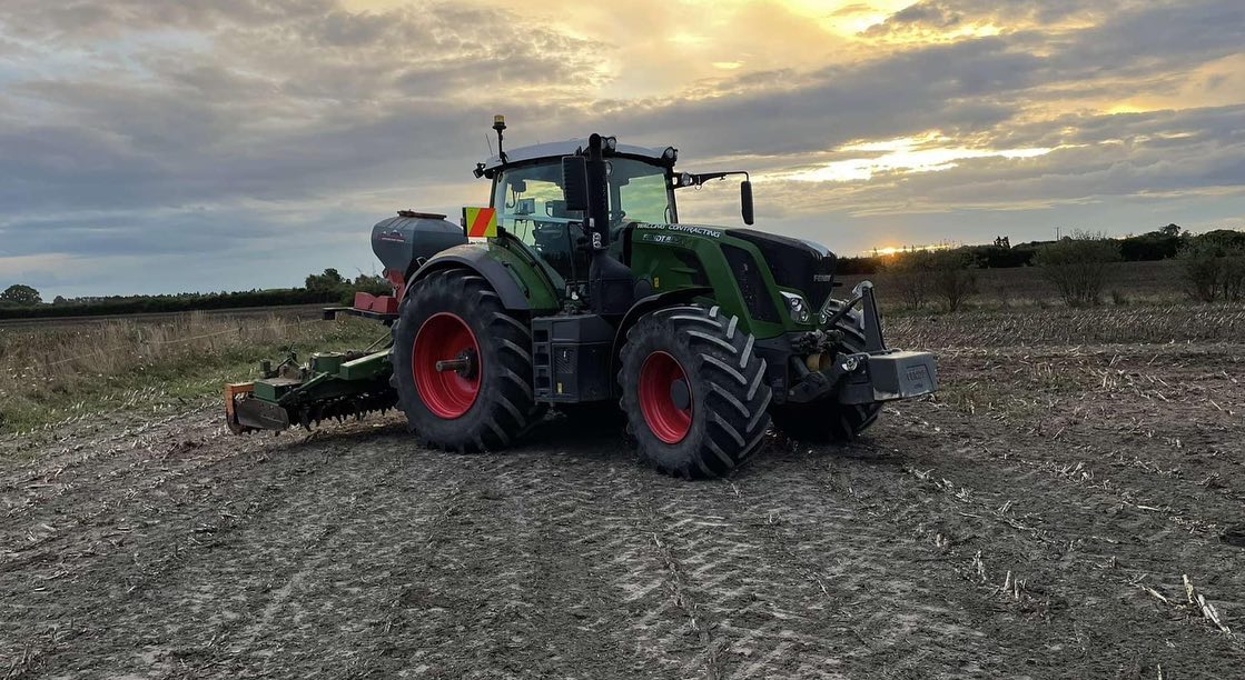 Fendt tractor with a power harrow and seed drill combination on cultivated ground at dusk, the sun low on the horizon under a cloudy sky